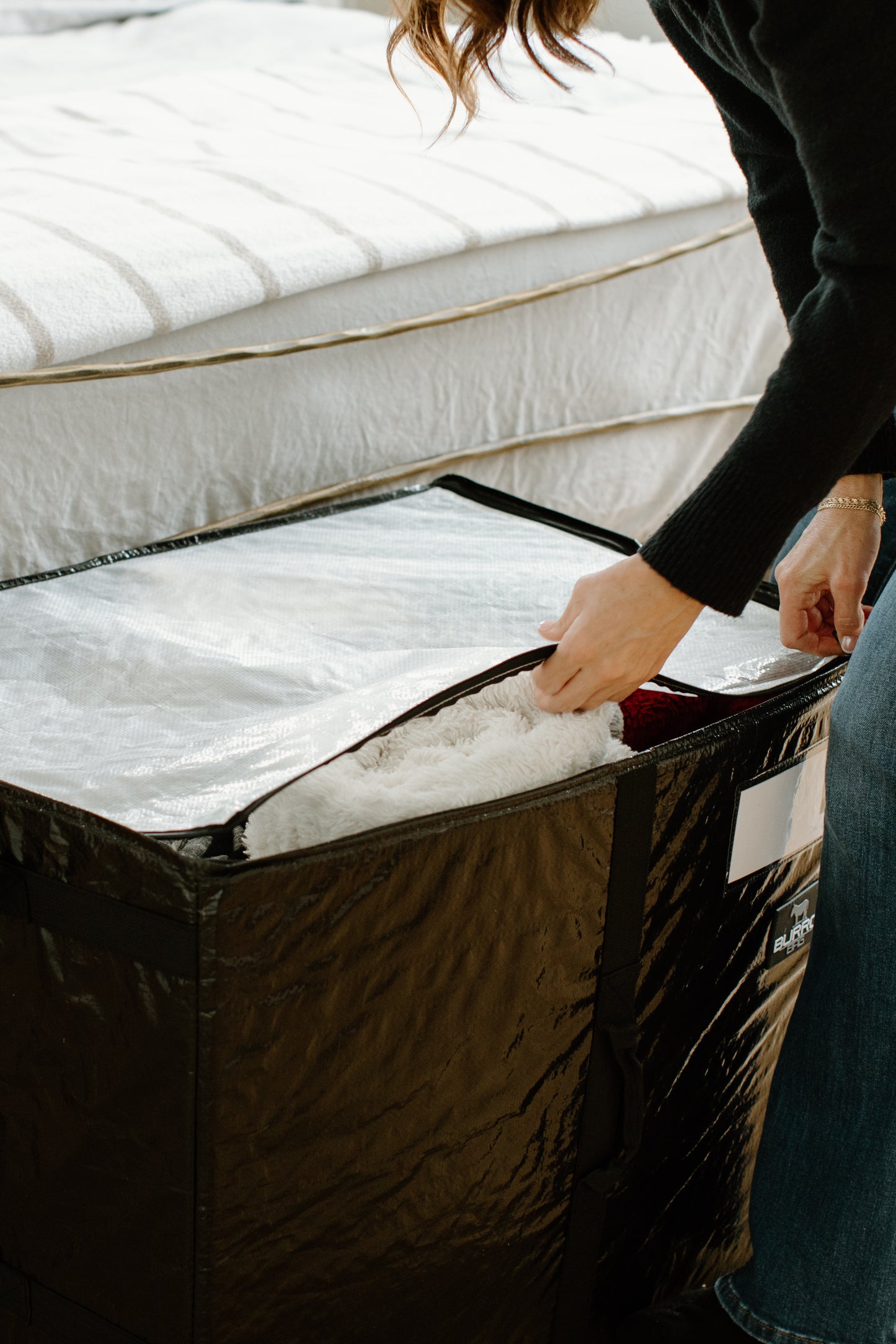A women effortlessly zipping up a Burro Bag, brimming with cozy blankets, highlighting its spaciousness and ease of use for various storage and organizational needs.